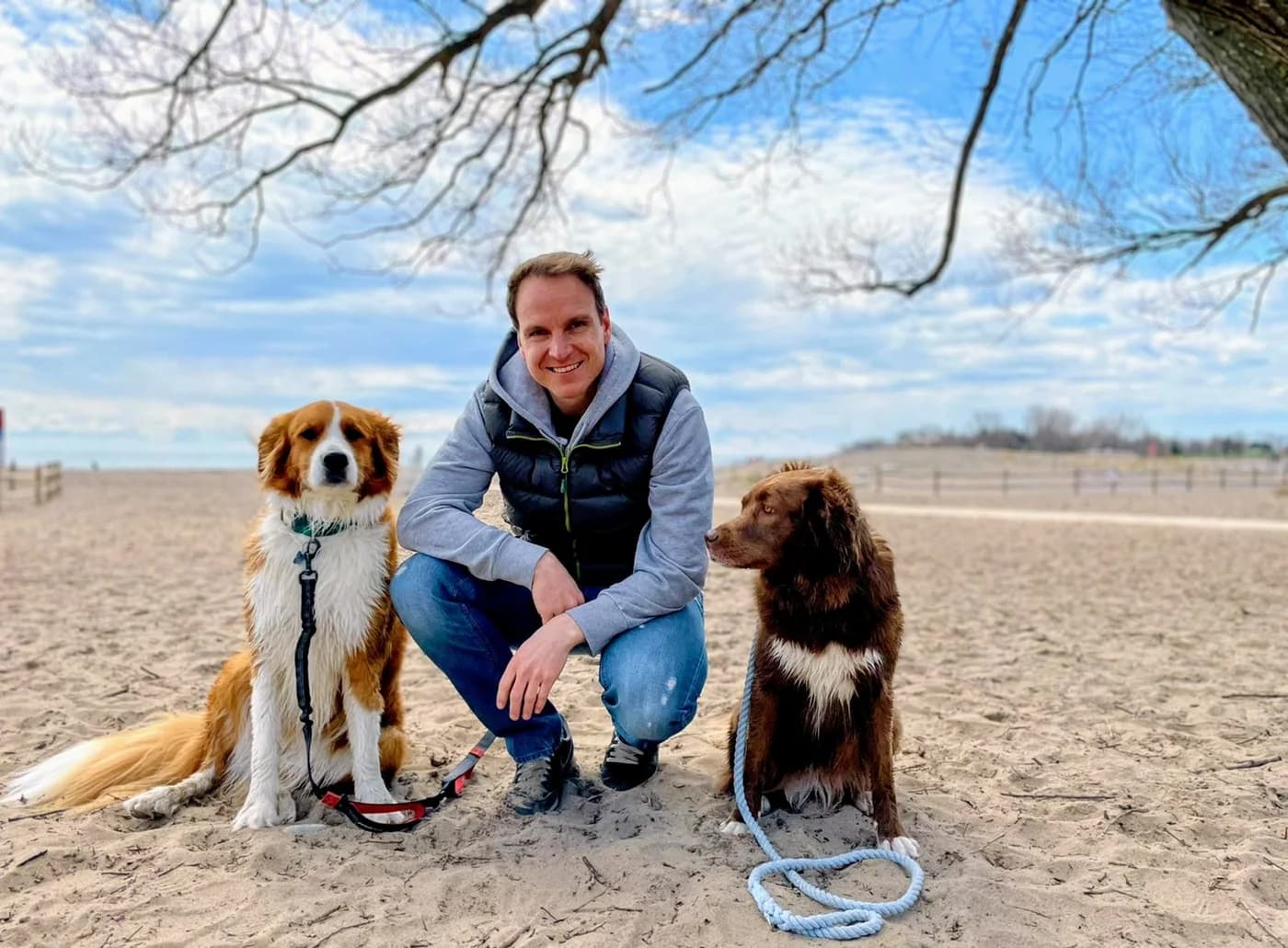 Marc kneeling on the beach between his two dogs, Roxy and Mittens